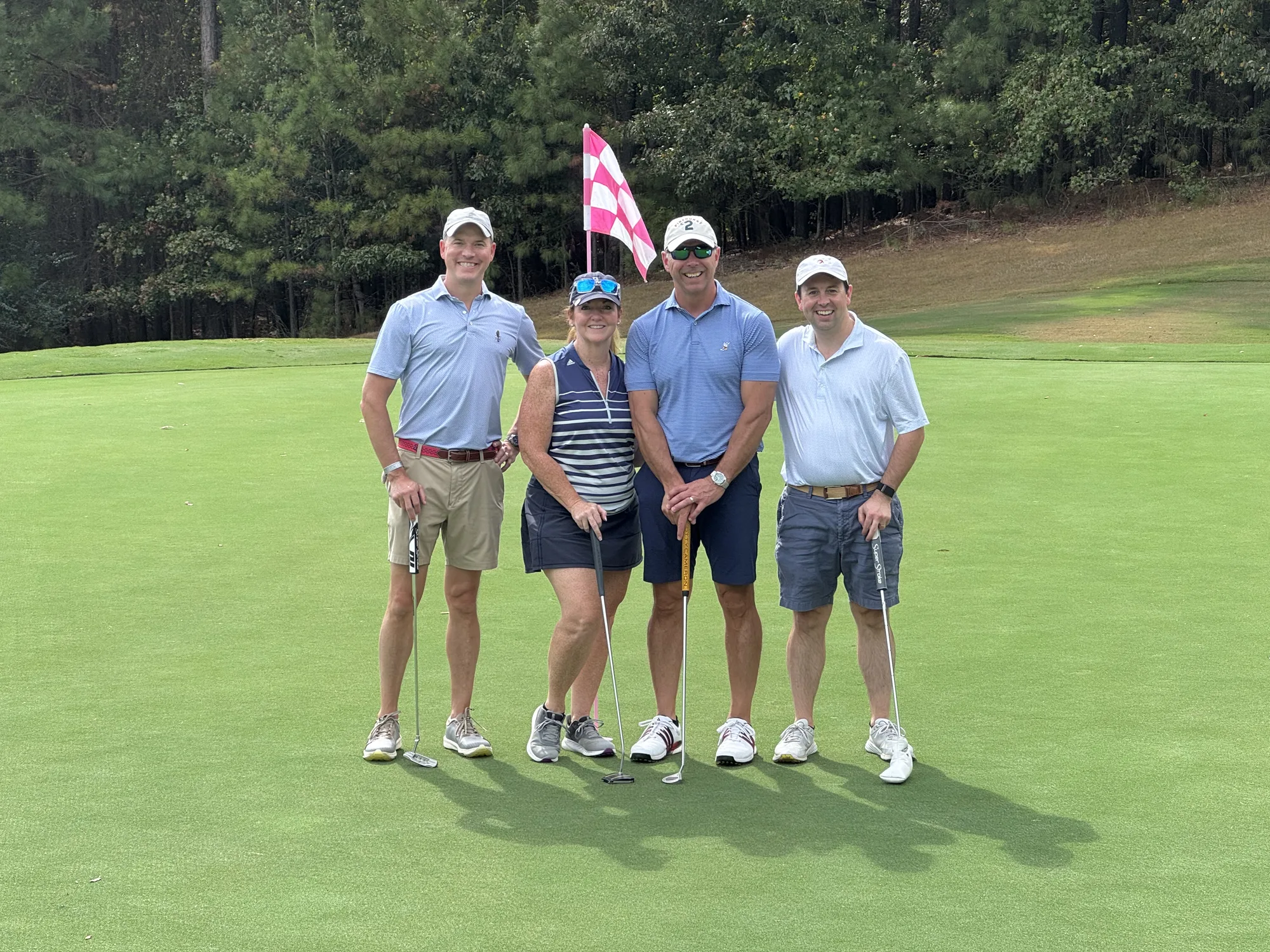 A foursome posing together with golf clubs on the course.
